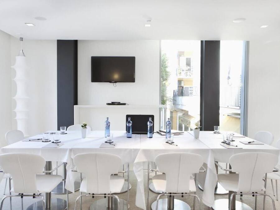 Une salle de conférence moderne, dotée d’une longue table, de chaises blanches, d’un téléviseur à écran plat et d’une cheminée.