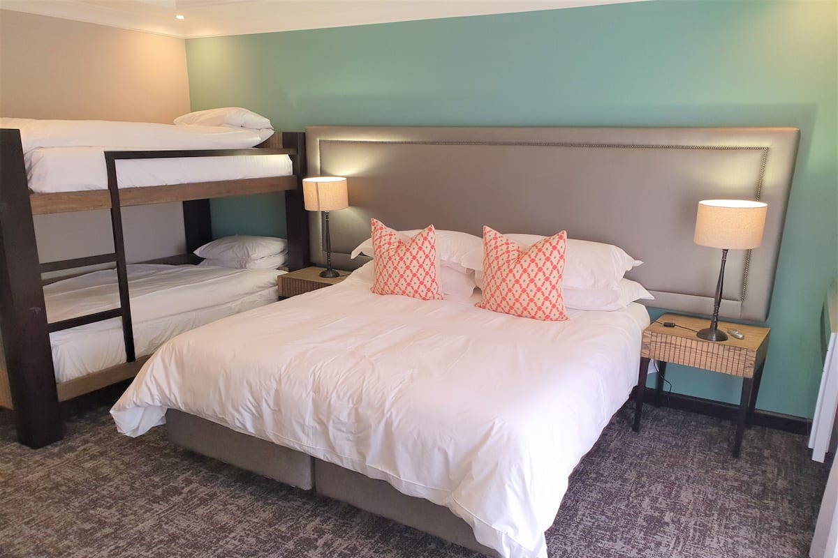 Habitación de hotel con una cama grande, una cama nido abajo, dos mesitas de noche con lámparas y una alfombra estampada.