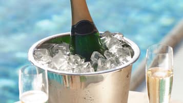 A metal bucket filled with ice and a champagne bottle, two glasses of champagne, and a cork on a table by a pool.