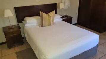 A neatly made bed with white linens and striped pillows, a bedside table with a lamp, and a small drawer.