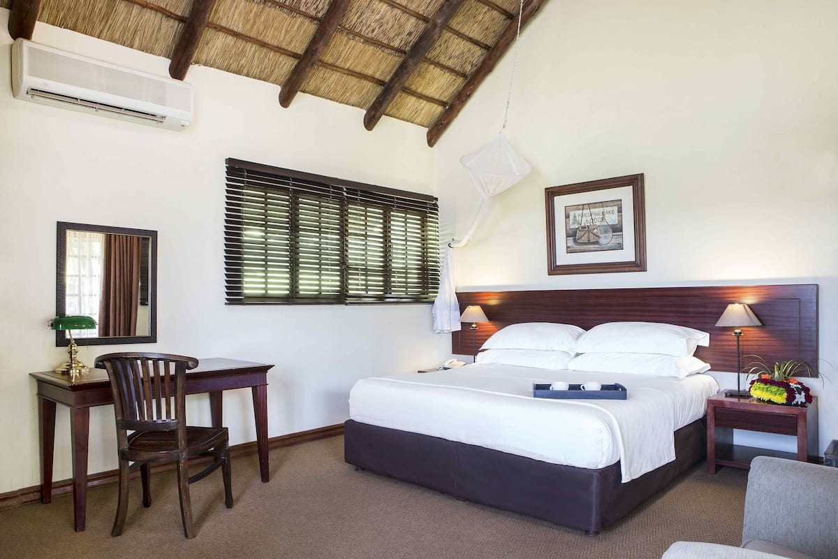 Habitación de hotel con cama, escritorio, silla y una mesita de noche con lámpara.