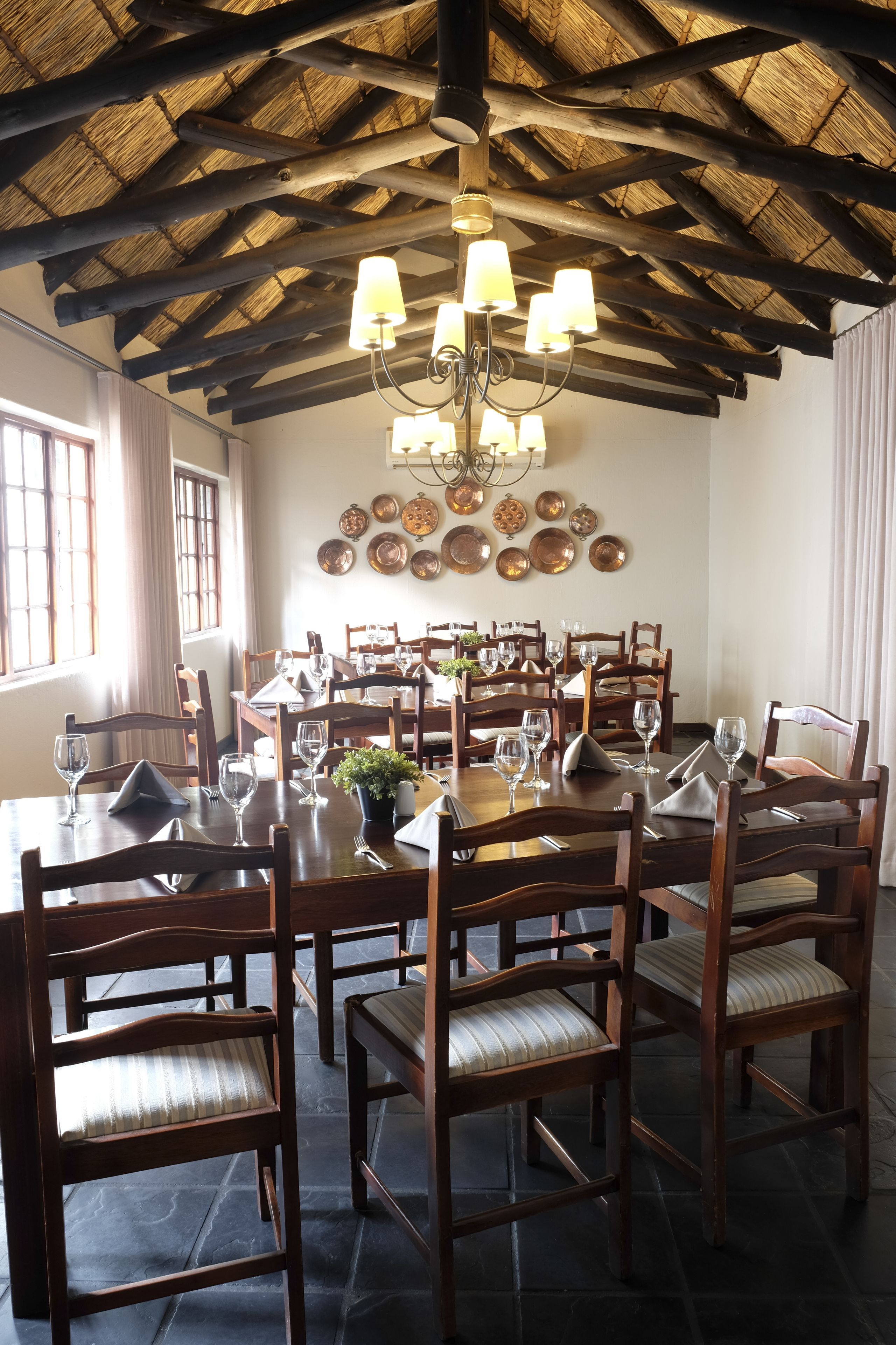 Uma sala de jantar com mesas e cadeiras de madeira, um candelabro e um teto de palha.