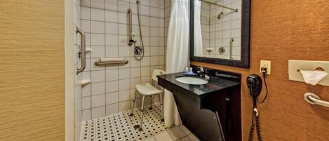 A bathroom with a shower, a toilet, a sink, a mirror, and a telephone.