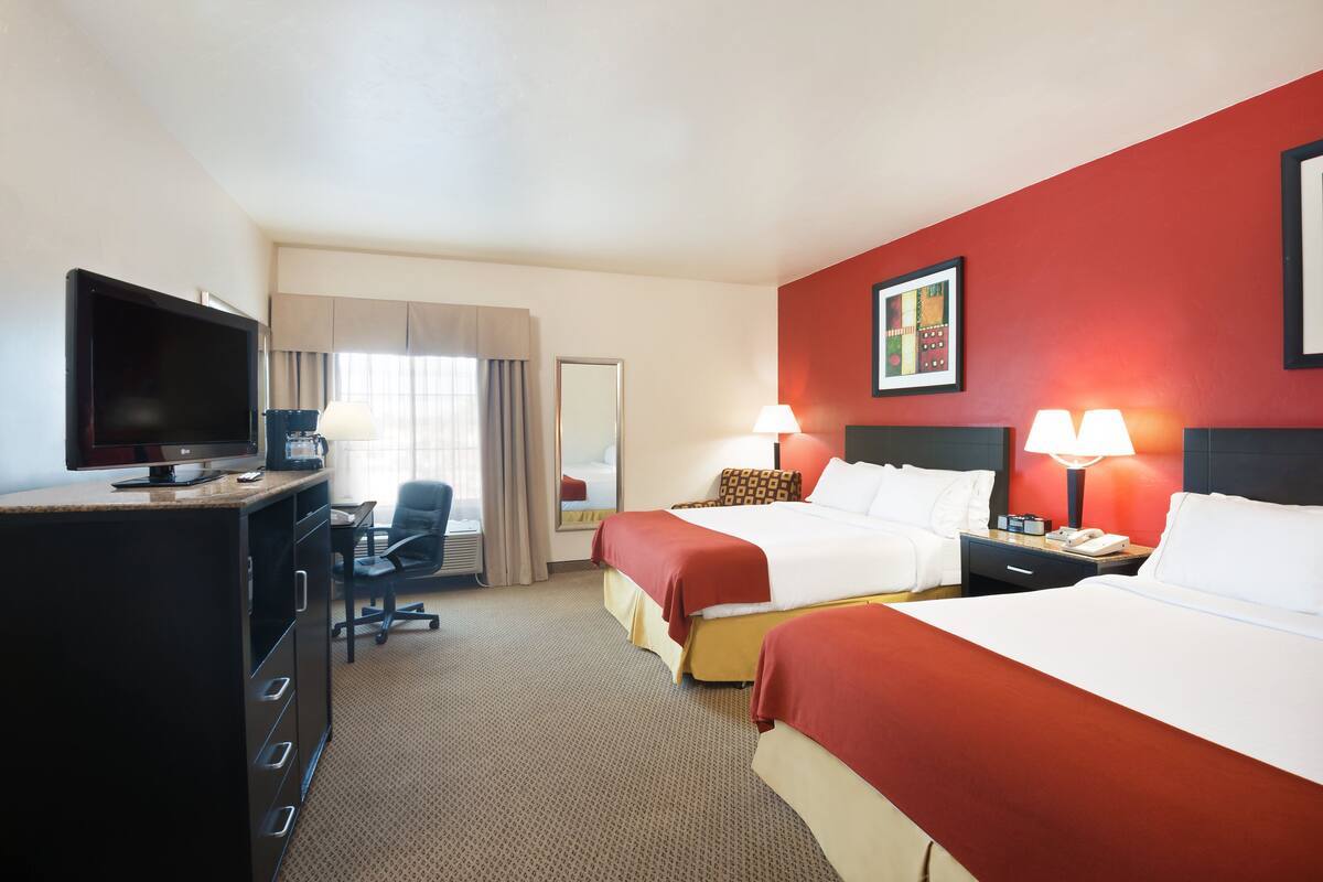 A hotel room with two beds, a desk with a TV, a chair, and a desk lamp.