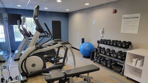 Un gimnasio con cintas de correr, una bicicleta estática, una máquina de remo, un balón de ejercicios azul y un soporte con mancuernas.