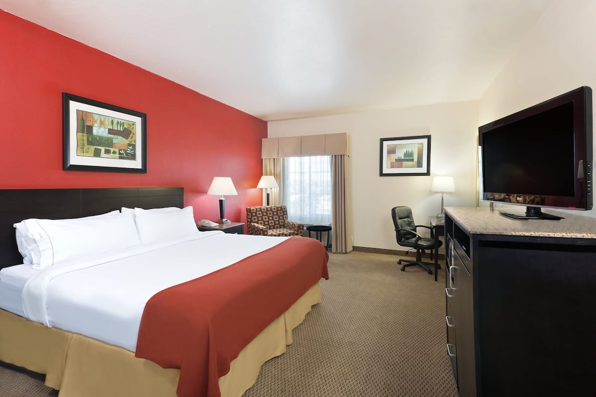 A hotel room with a large bed, a desk with a flat-screen TV, a chair, a lamp, and a framed picture on the wall.