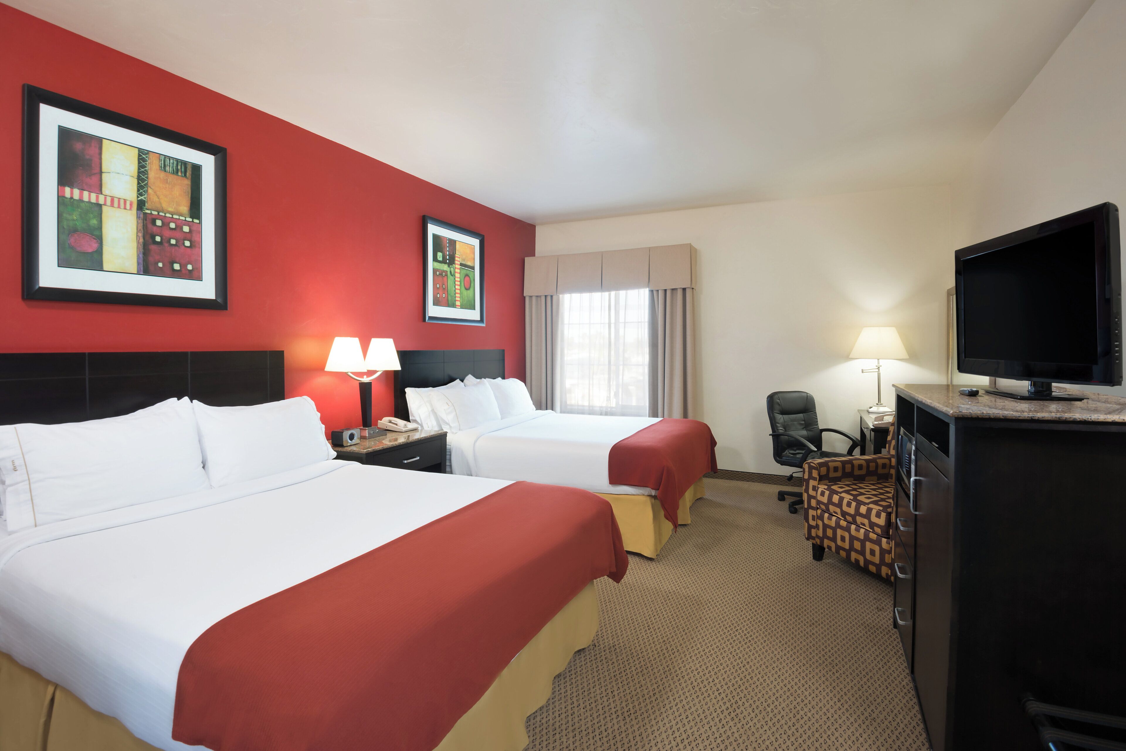 A hotel room with two beds, a television, a desk with a chair, and artwork on the walls.