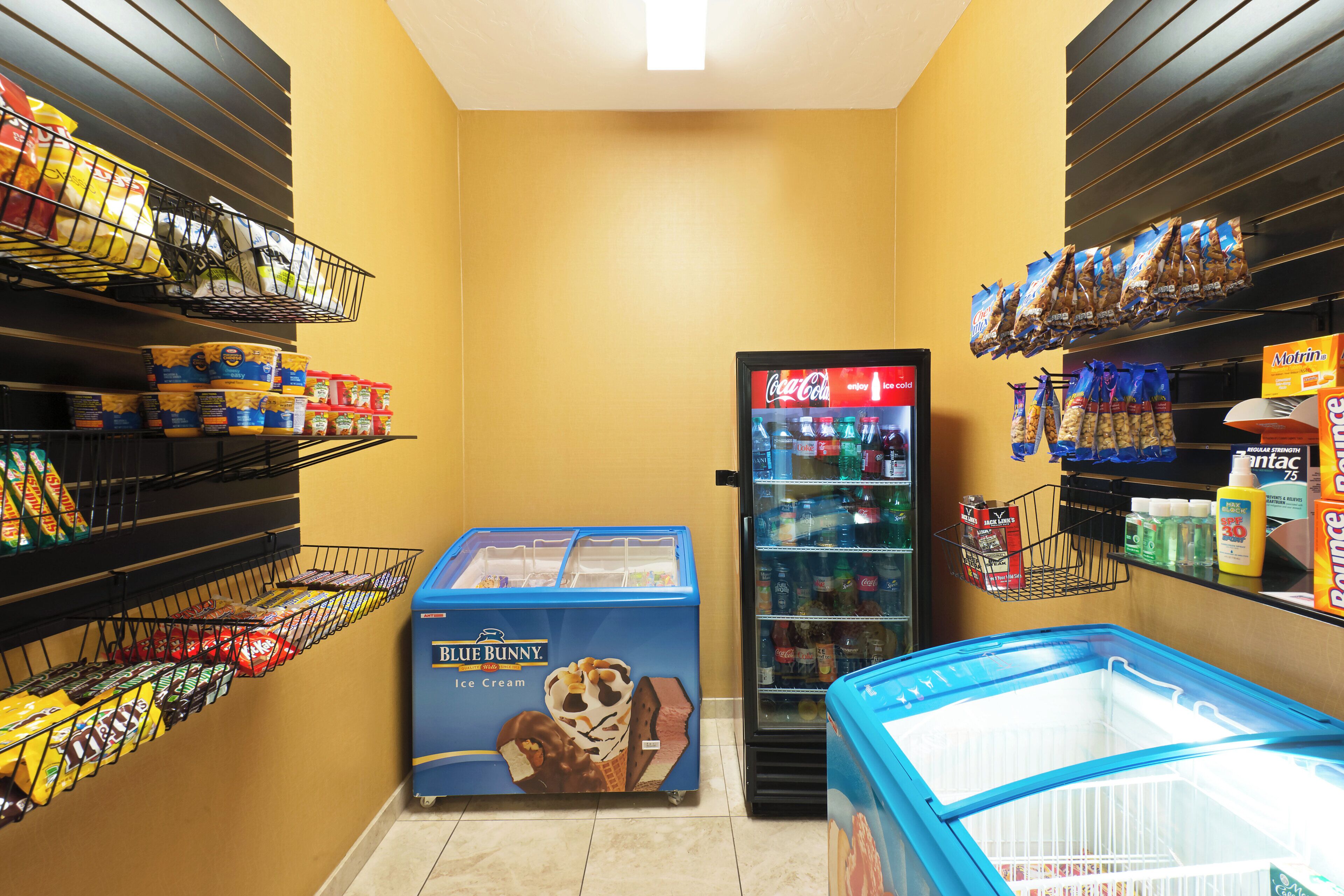 A grocery store with shelves stocked with snacks, a freezer with ice cream, and a refrigerator with beverages.
