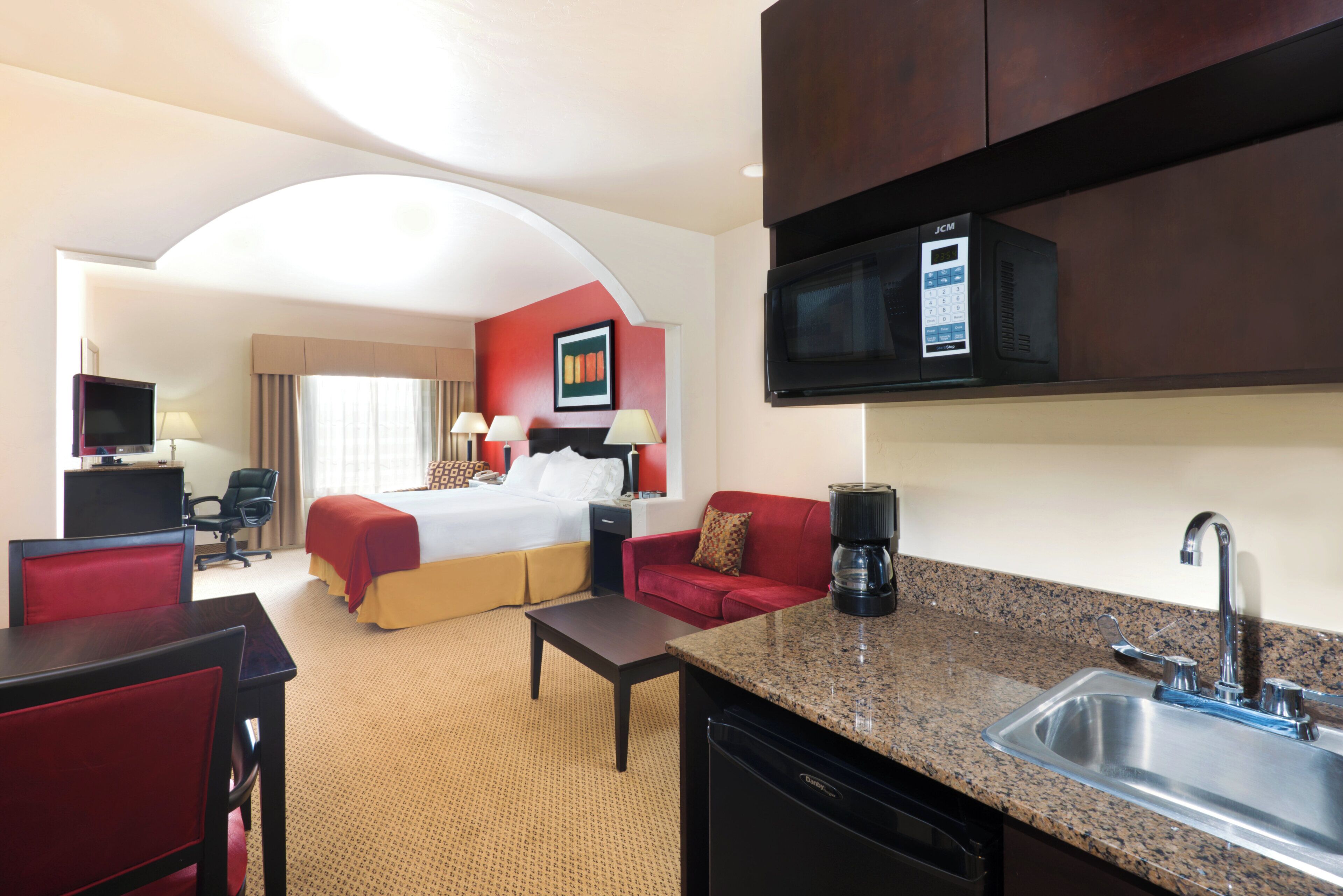 Habitación de hotel con cama, escritorio, cafetera, lavamanos y microondas.