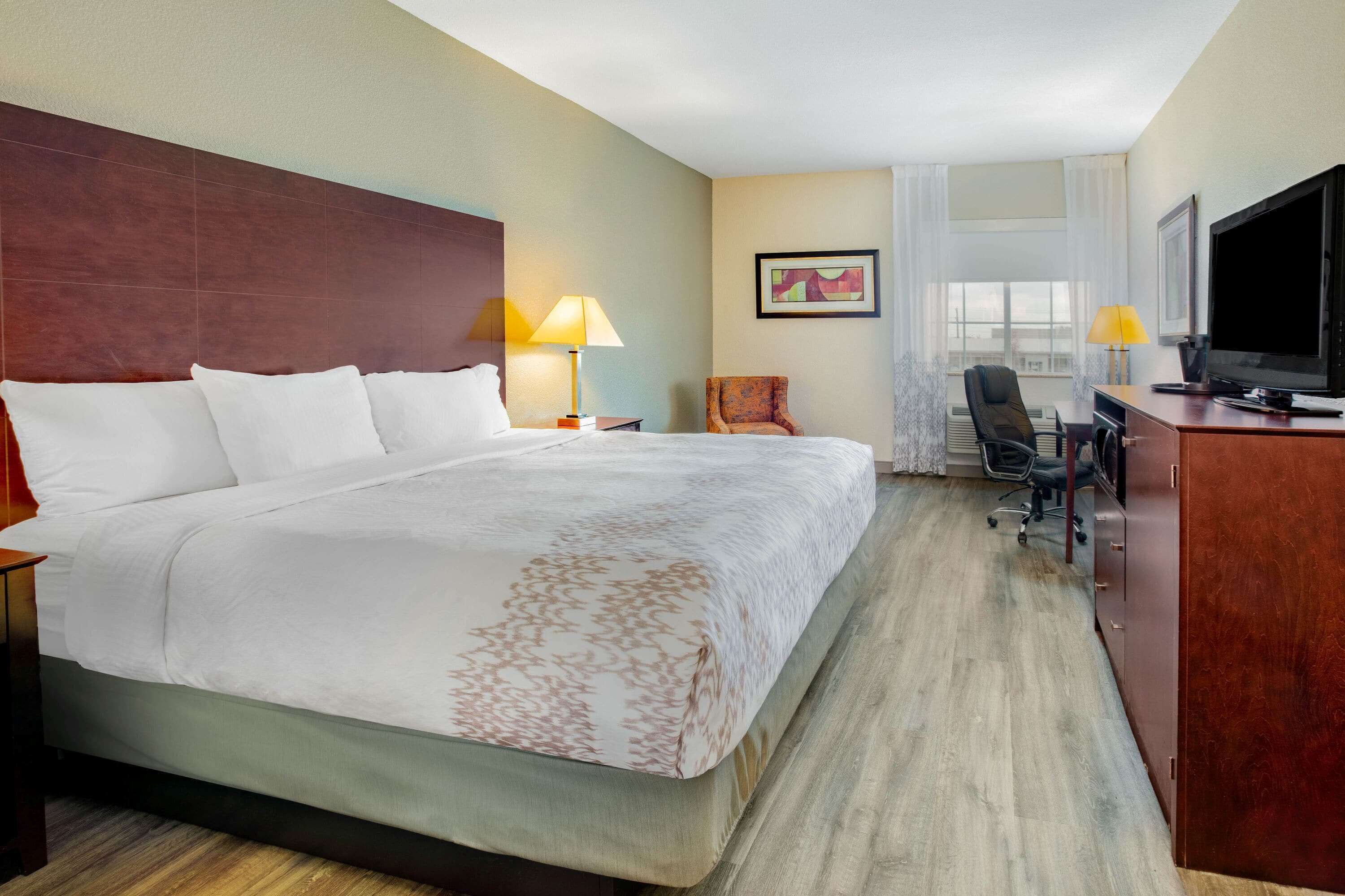 A hotel room with a large bed, a desk with a chair, a television, and a window with curtains.