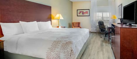 A hotel room with a large bed, a desk with a chair, a television, and a window with curtains.