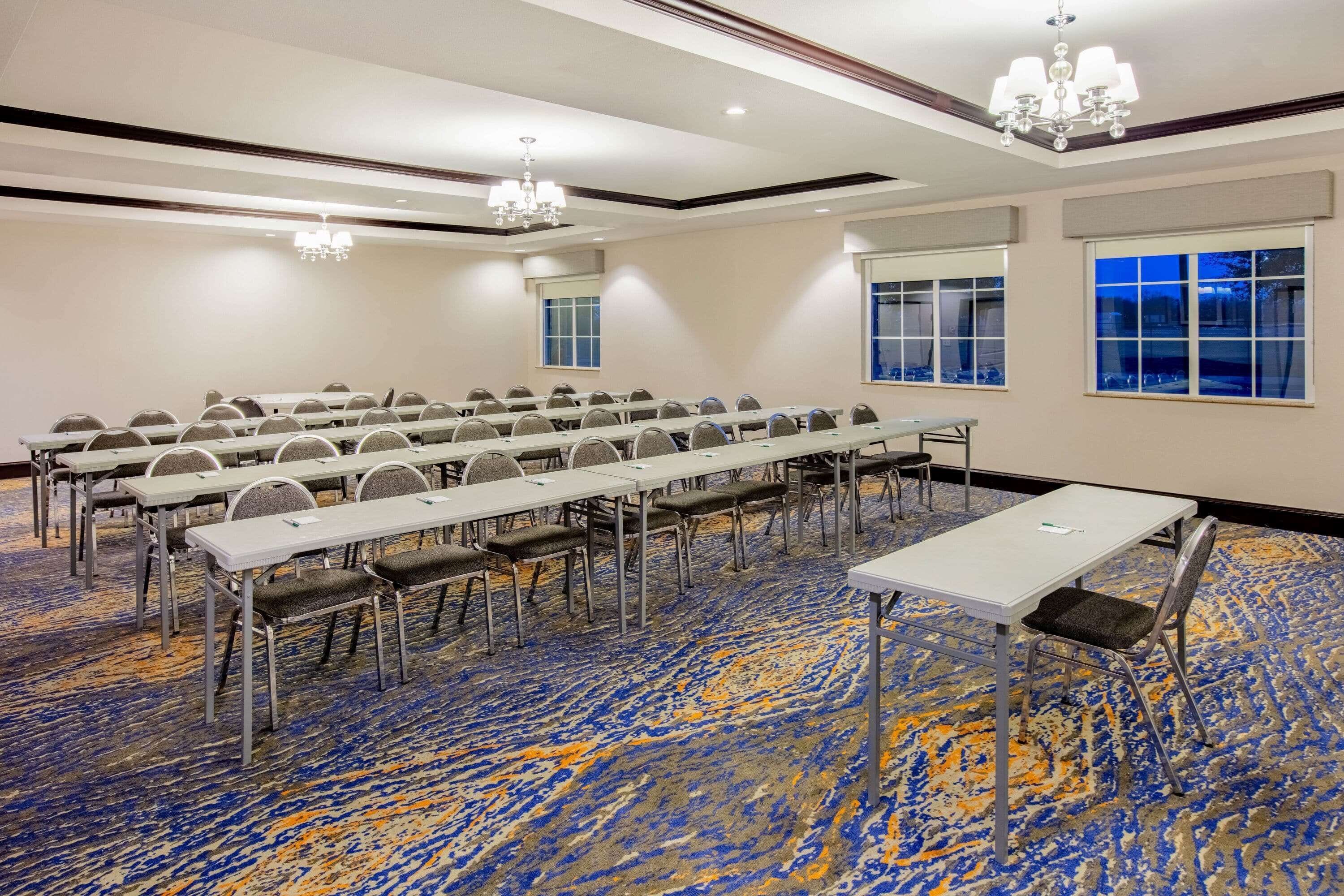Un salón de conferencias con largas mesas y sillas, amplias ventanas y una alfombra estampada.