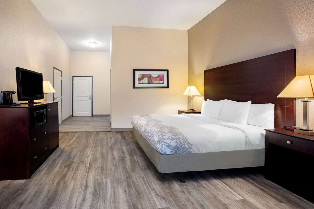 Ein Hotelzimmer mit einem Bett, Nachttischlampen, einem Fernseher und einem kleinen Schreibtisch mit Lampe.