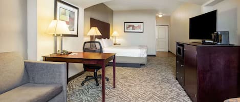 A hotel room with a bed, a desk, a chair, a sofa, a television, and a minibar.