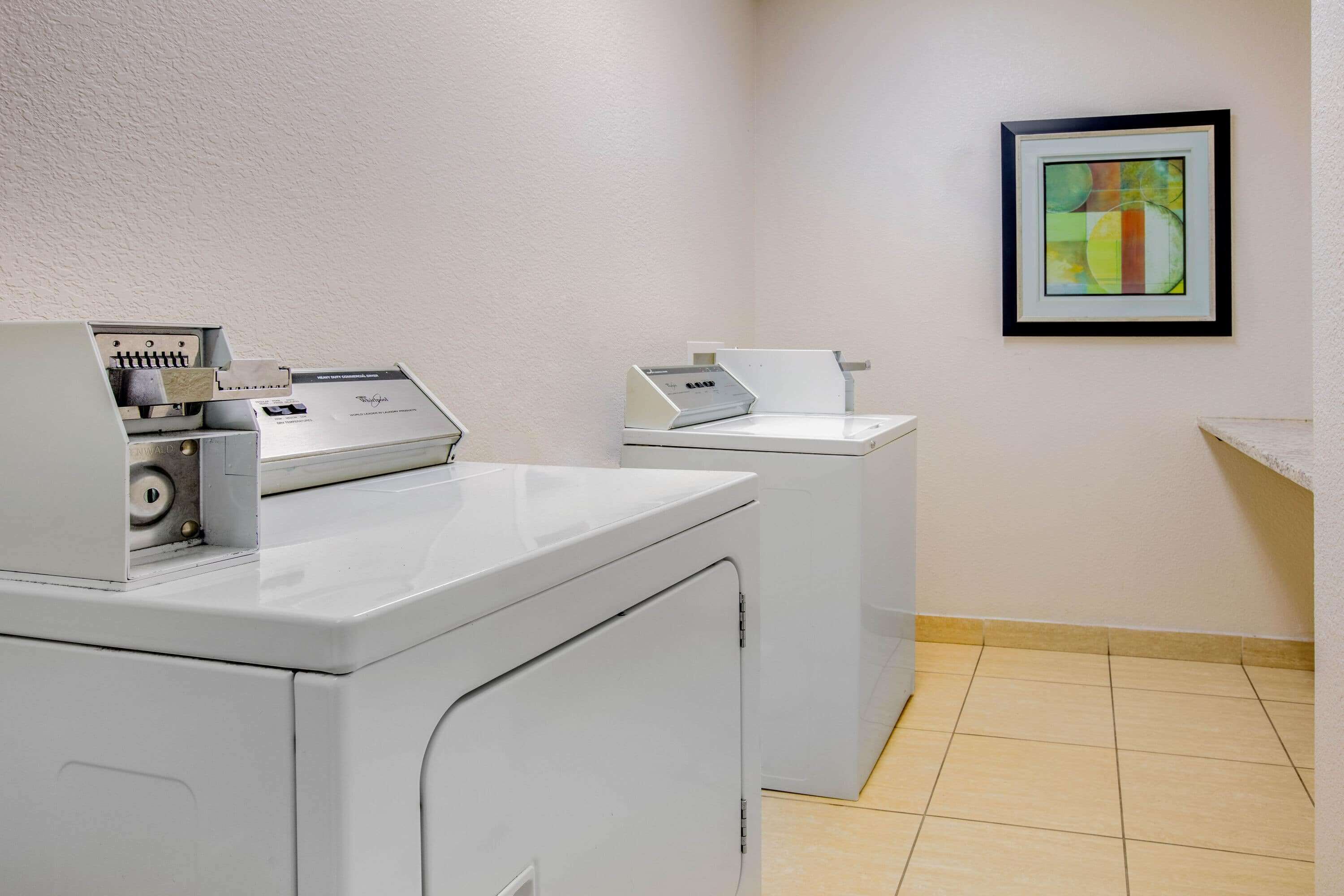 Une buanderie équipée de deux machines à laver blanches et ornée d’un tableau abstrait encadré au mur.