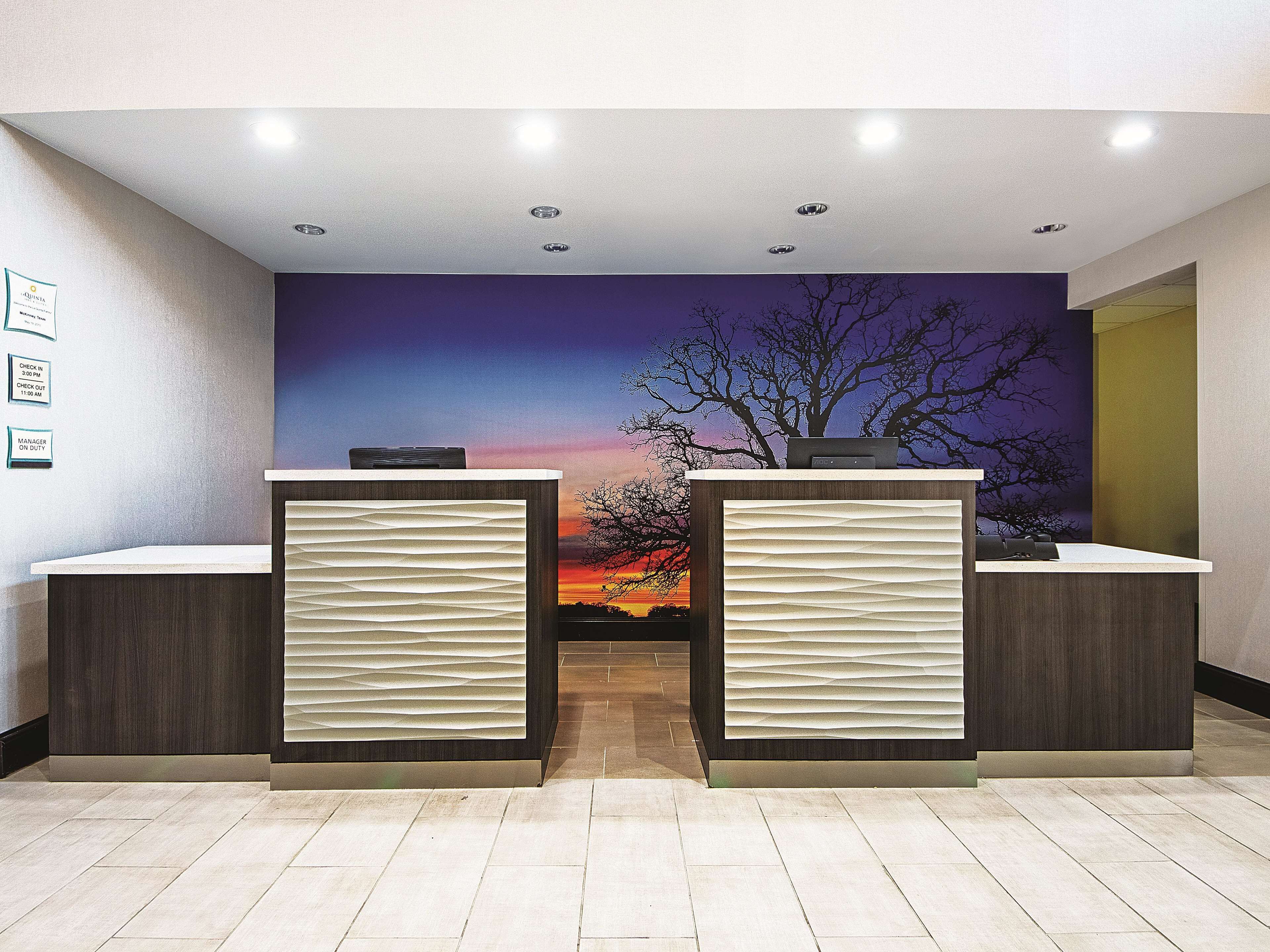 Un mostrador de recepción de diseño moderno, con una pantalla digital y un mural de atardecer.