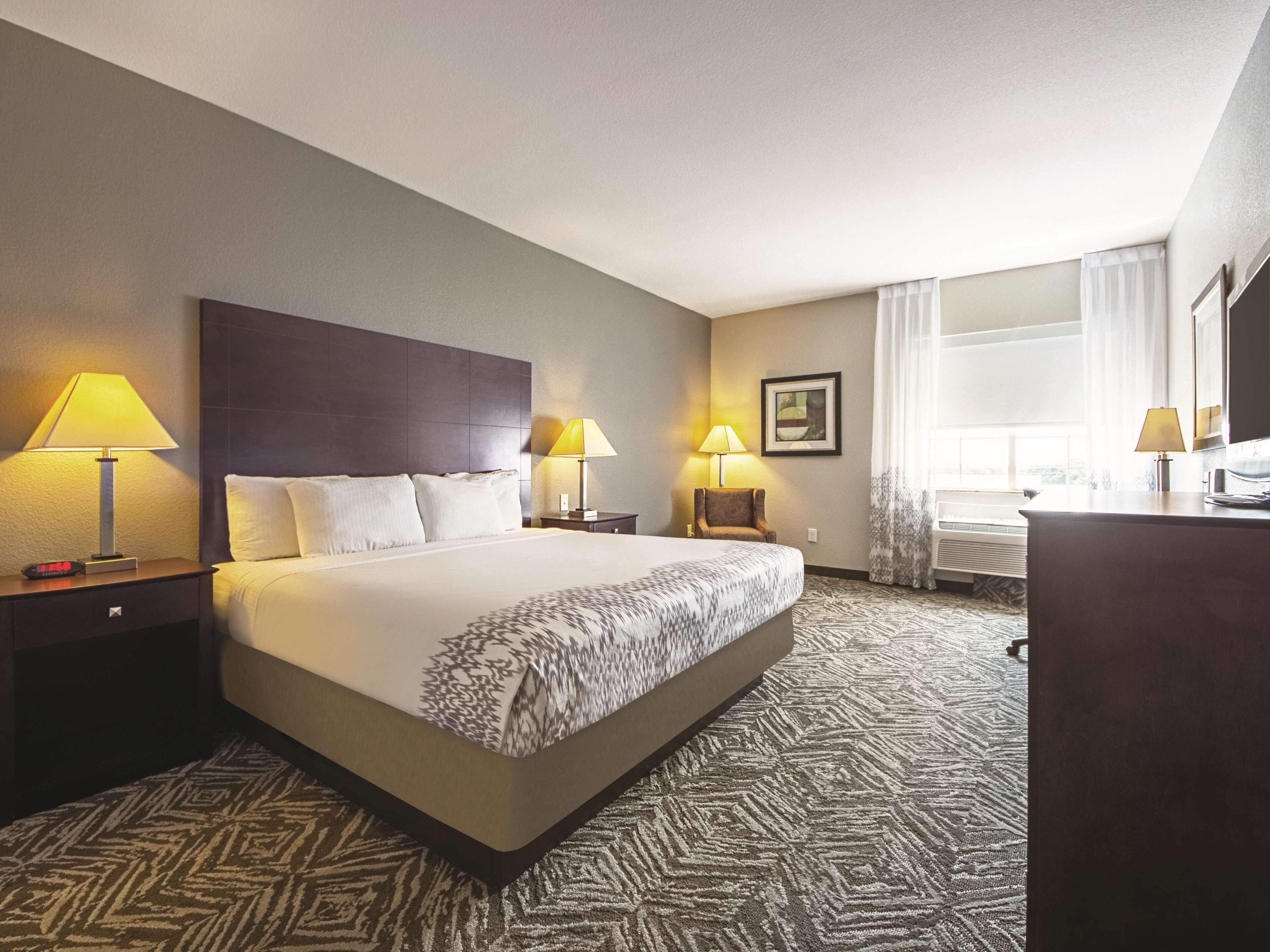 A hotel room with a large bed, two bedside tables with lamps, a desk with a chair, and a window with curtains.