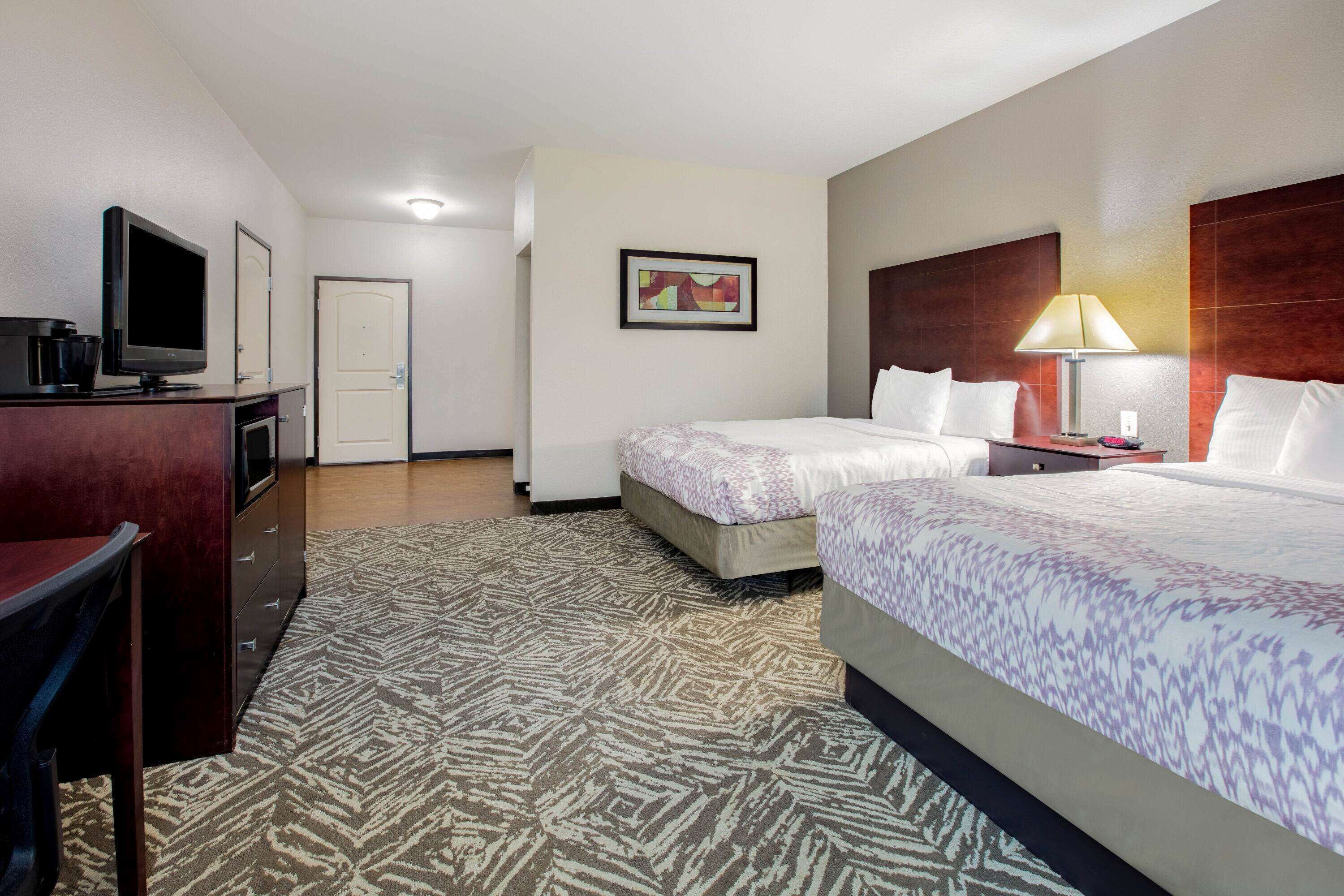 A hotel room with two beds, a desk, a television, a lamp, and a framed picture on the wall.