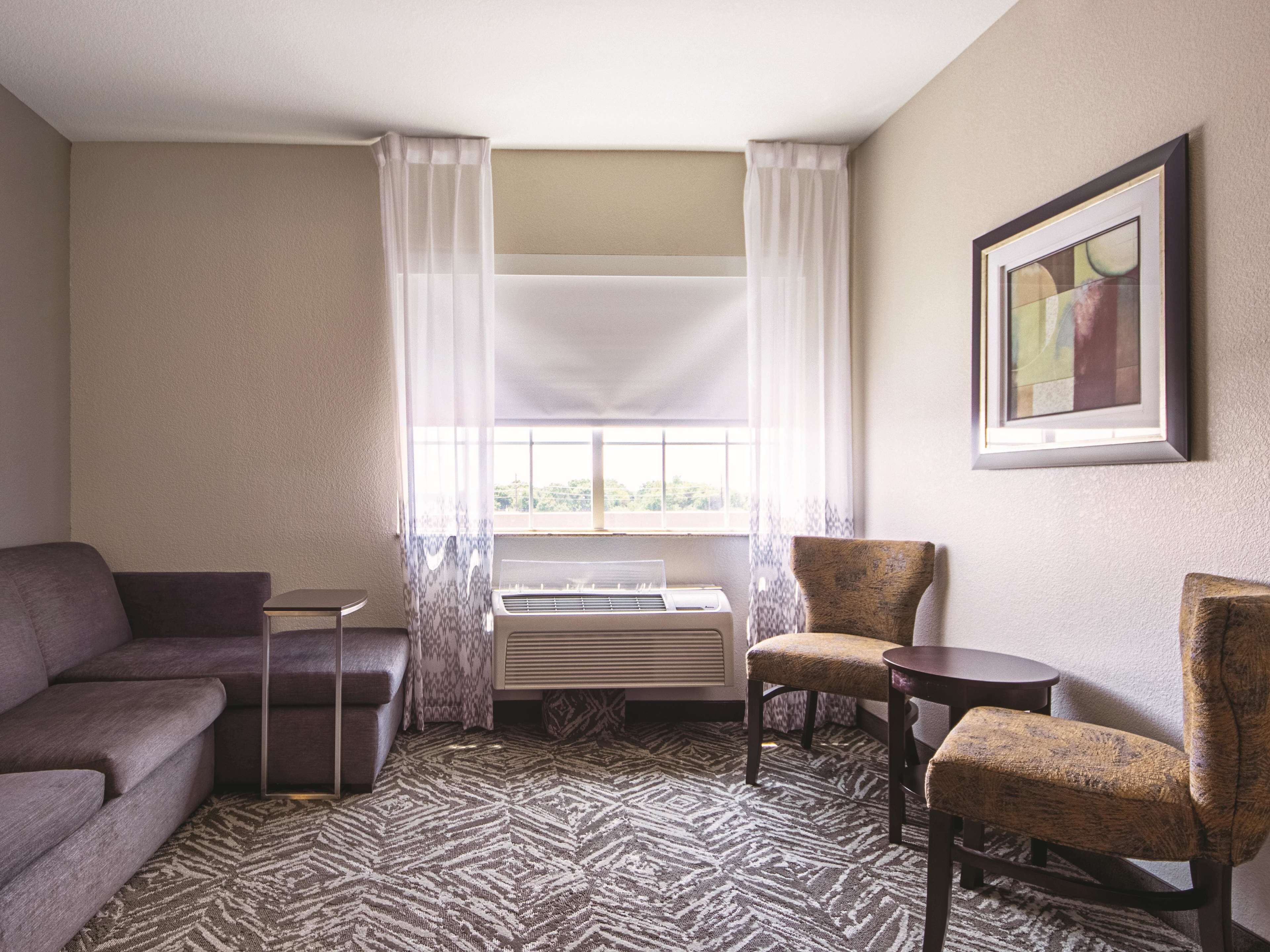 Une chambre d’hôtel avec un canapé, deux fauteuils, une petite table, un radiateur et une fenêtre avec des rideaux.