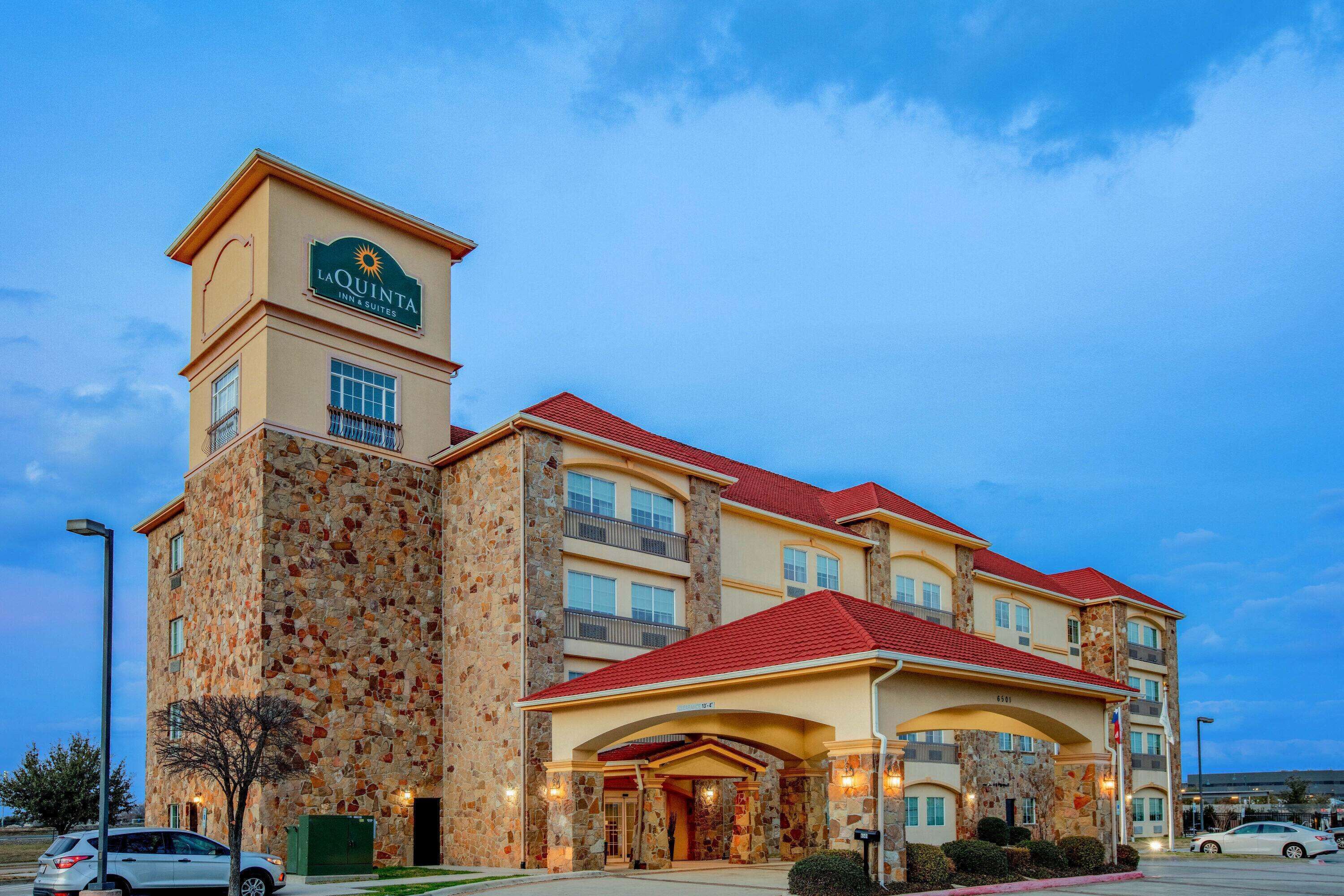 A multi-story hotel with a stone facade, red roof, and a sign indicating it is a La Quinta Inn & Suites.