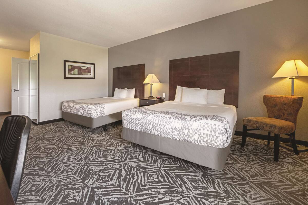 Ein Hotelzimmer mit zwei Betten, einem Schreibtisch, einem Stuhl und einer Lampe.