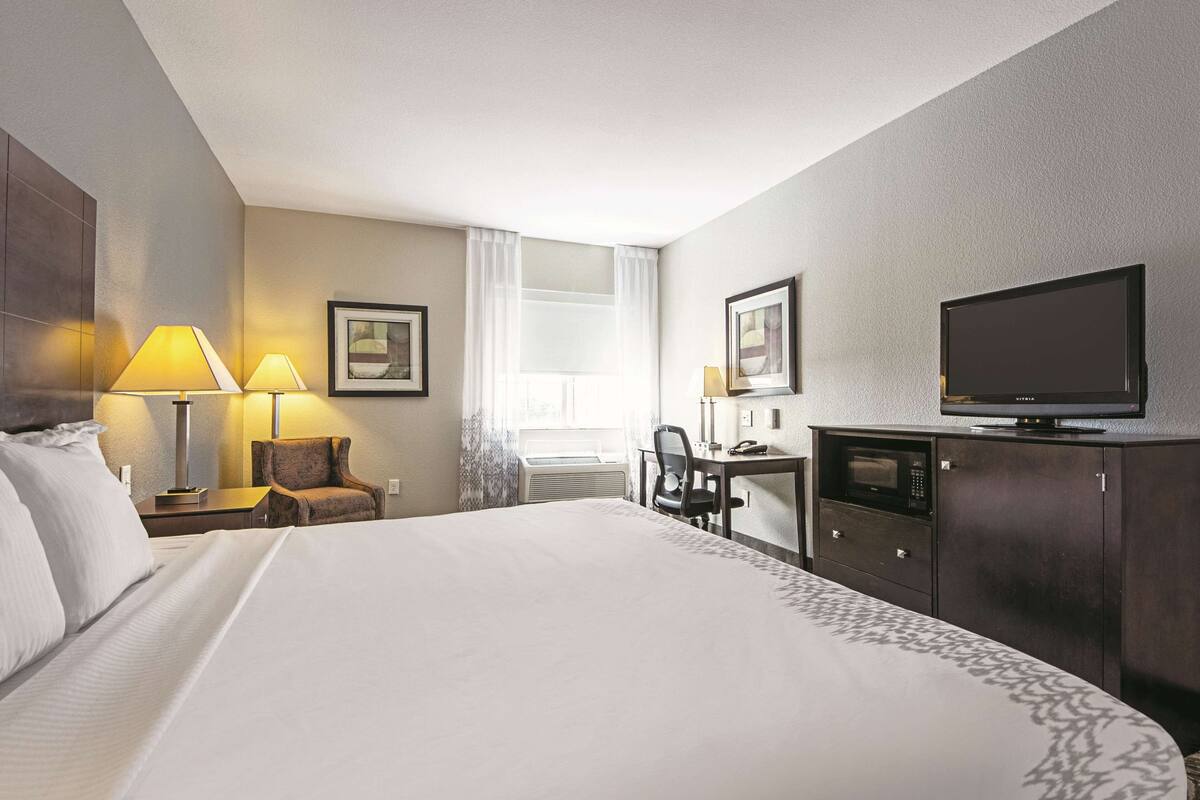 Ein Hotelzimmer mit einem großen Bett, zwei Nachttischlampen, einem Schreibtisch mit Stuhl, einem Fernseher und gerahmten Kunstwerken an den Wänden.
