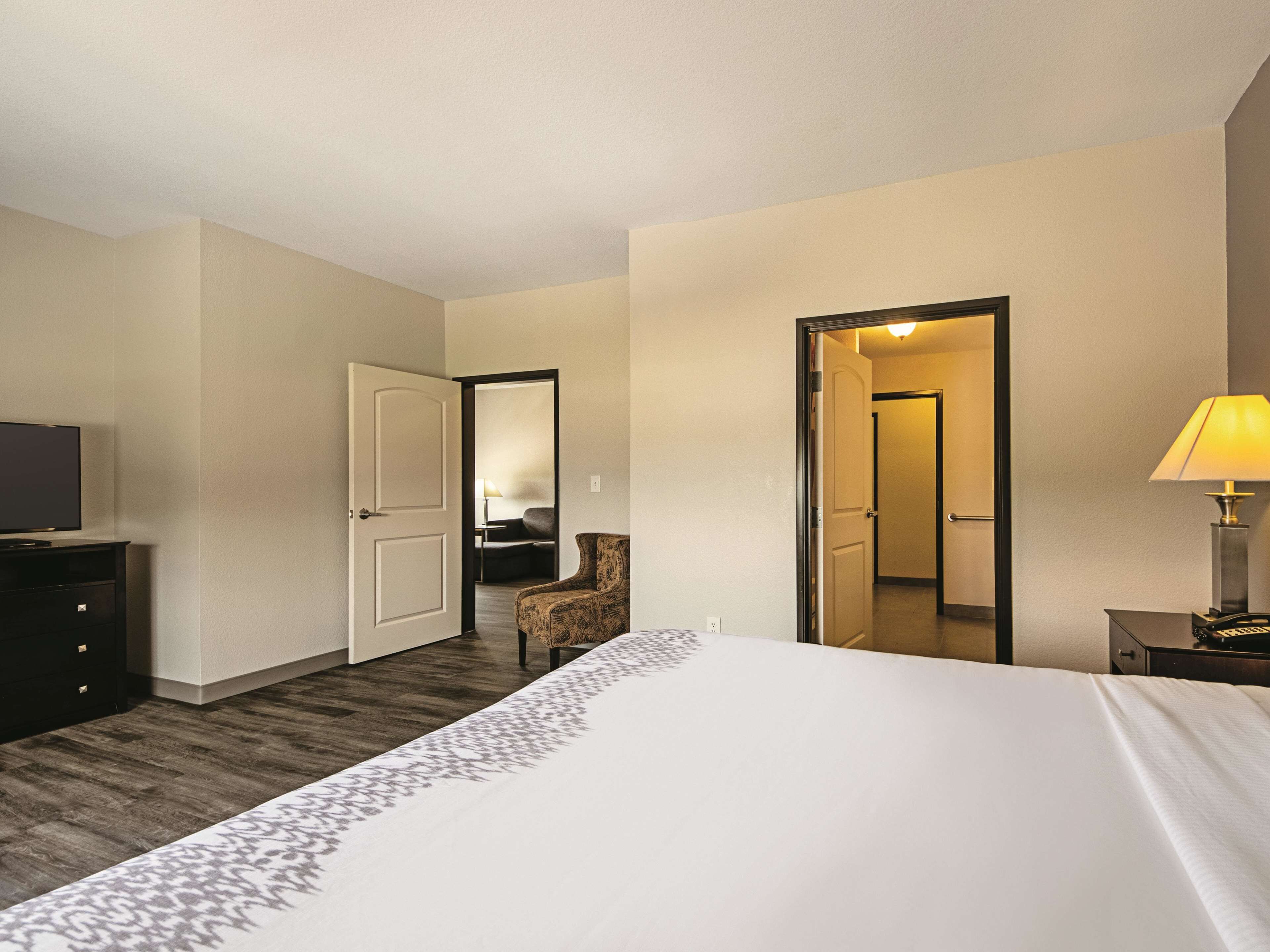 A hotel room with a bed, a TV, a desk with a lamp, and a chair.