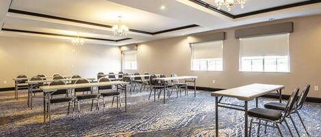 A conference room with a carpeted floor, tables, chairs, and two chandeliers.