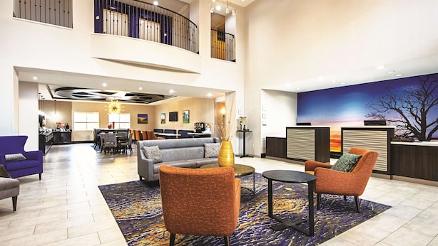 A spacious lobby with a high ceiling, a reception desk, a seating area with sofas and chairs, and a view of the sky through a large window. - La Quinta Inn & Suites by Wyndham McKinney (McKinney)