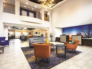 A spacious lobby with a high ceiling, a reception desk, a seating area with sofas and chairs, and a view of the sky through a large window. - La Quinta Inn & Suites by Wyndham McKinney (McKinney)