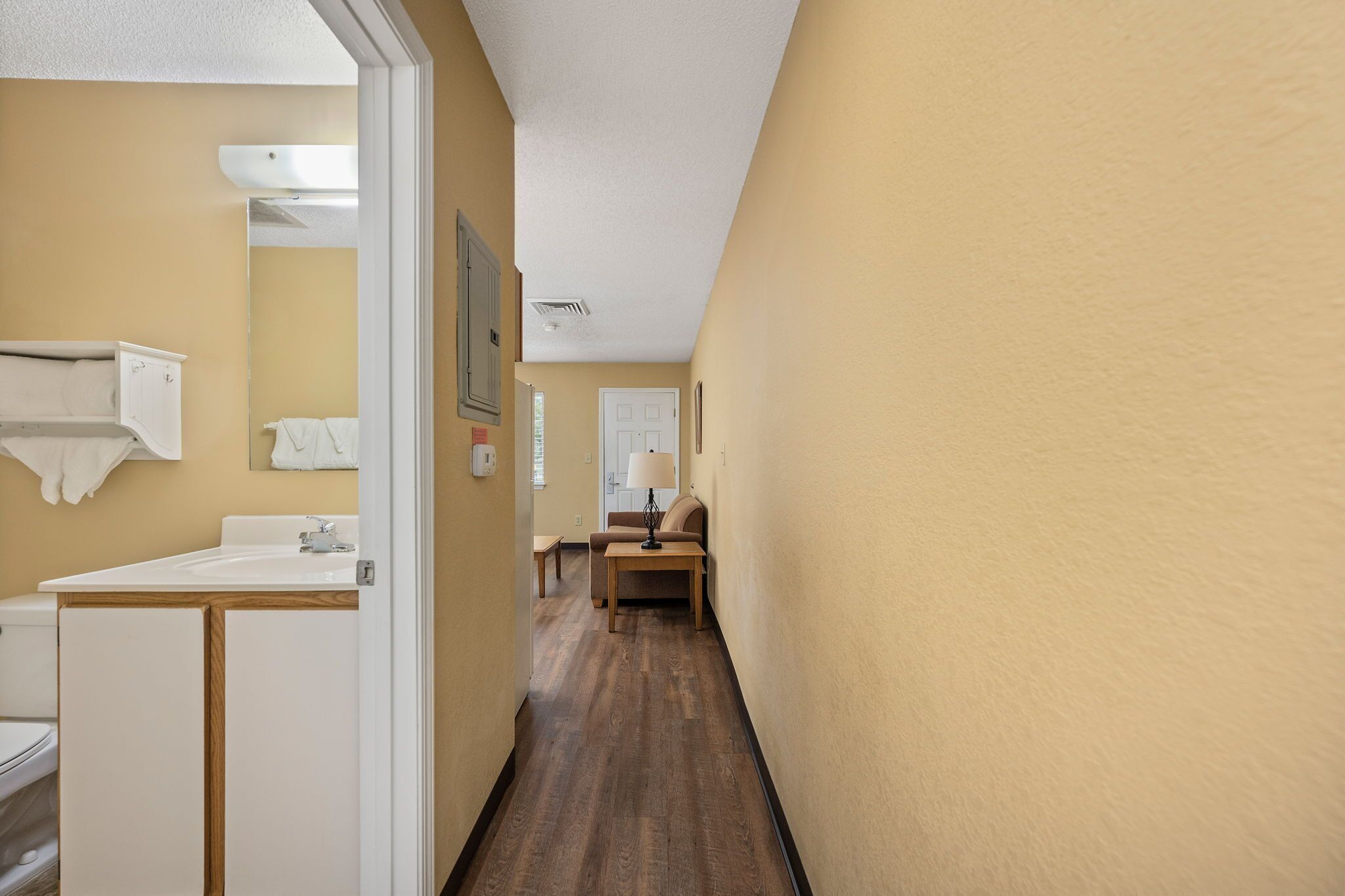A narrow hallway with a wooden floor, a white sink, and a beige wall.
