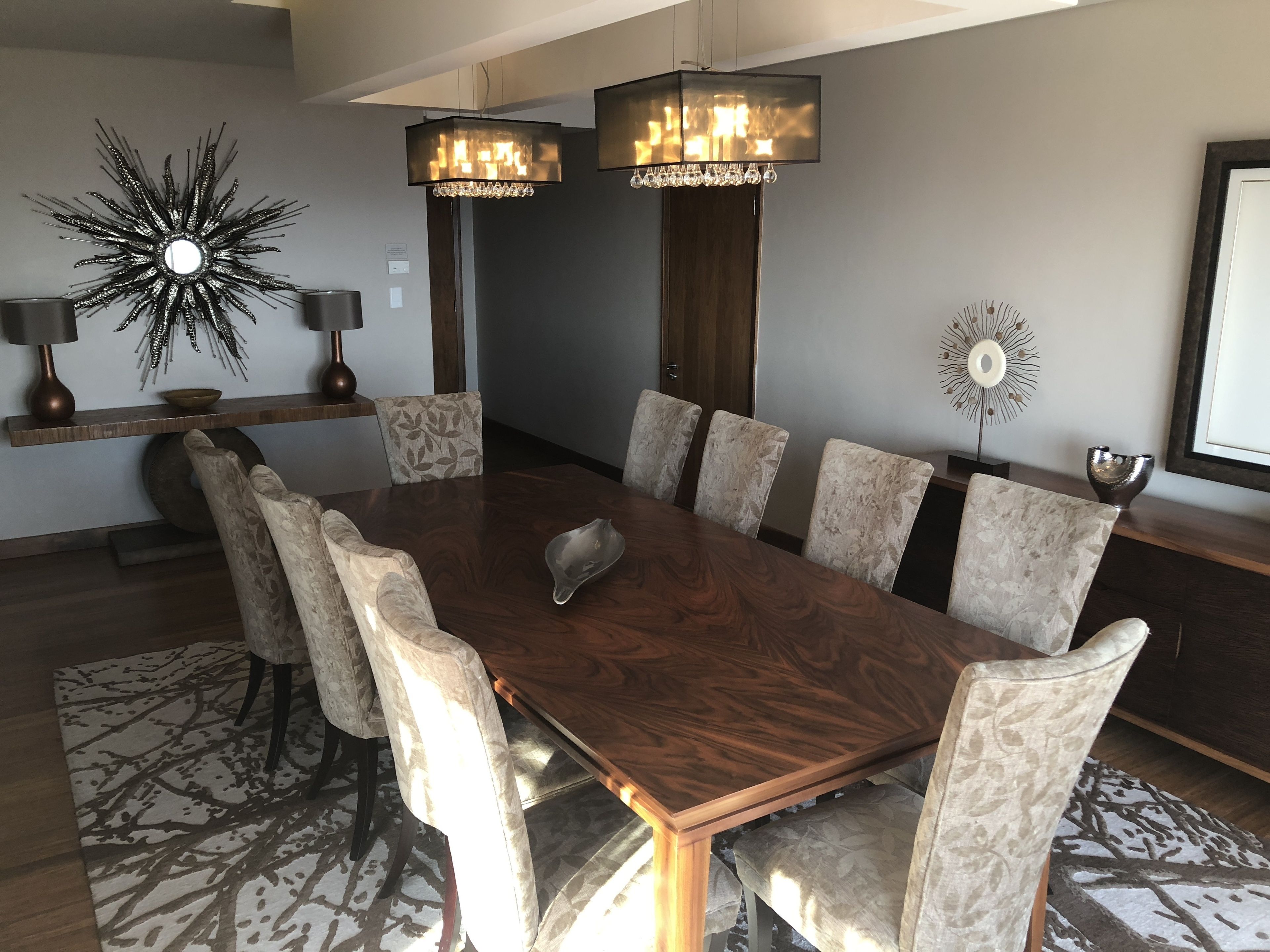 A modern dining room with a large wooden table, patterned chairs, and decorative lighting fixtures.