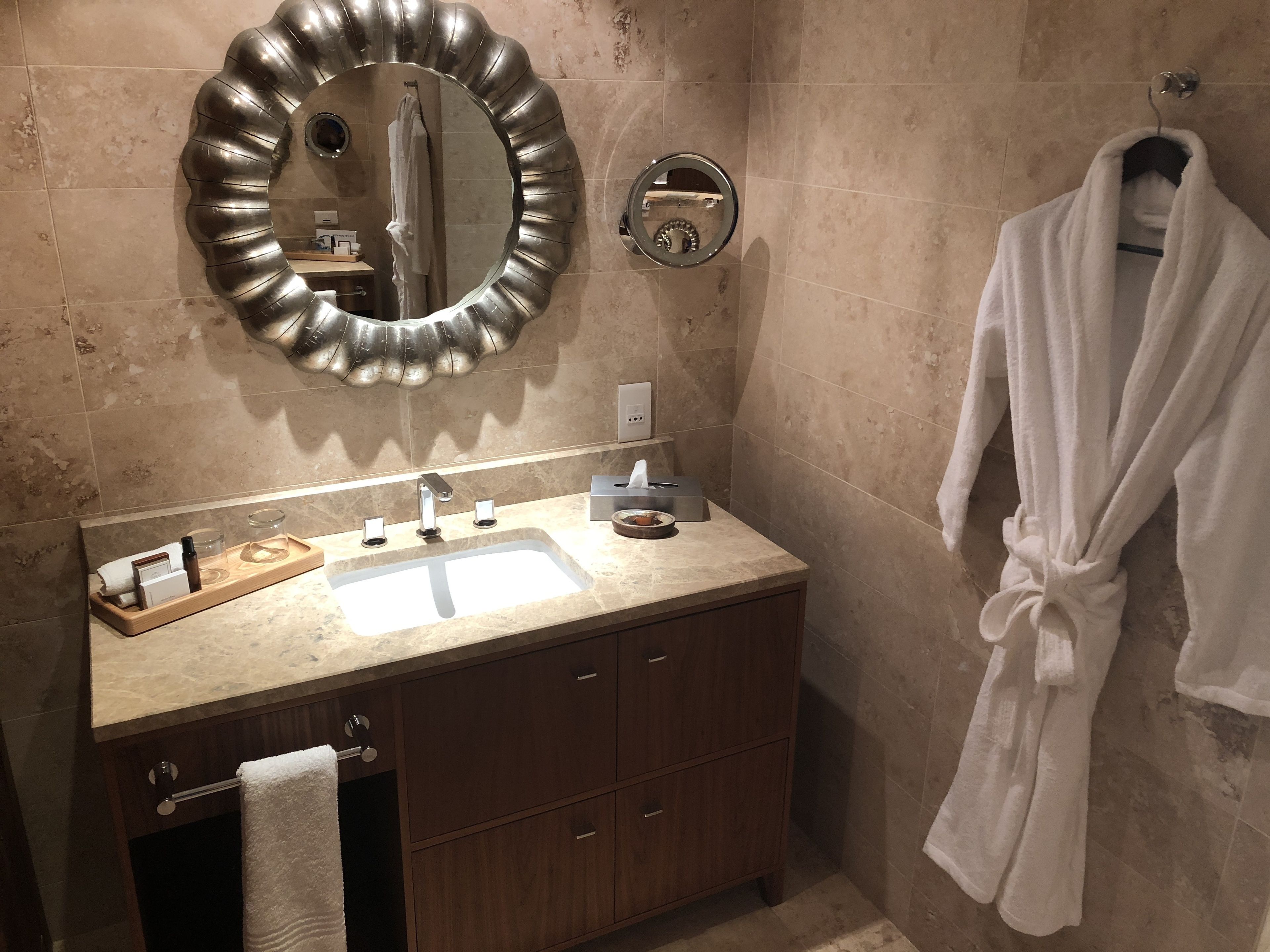 A bathroom with a vanity, a mirror, a towel rack, and a robe hanging on the wall.