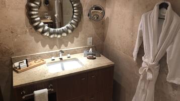 A bathroom with a vanity, a mirror, a towel rack, and a robe hanging on the wall.