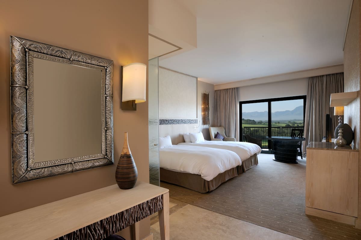 Une chambre d’hôtel avec un grand miroir, un vase, un lit, un bureau et une vue sur l’extérieur.