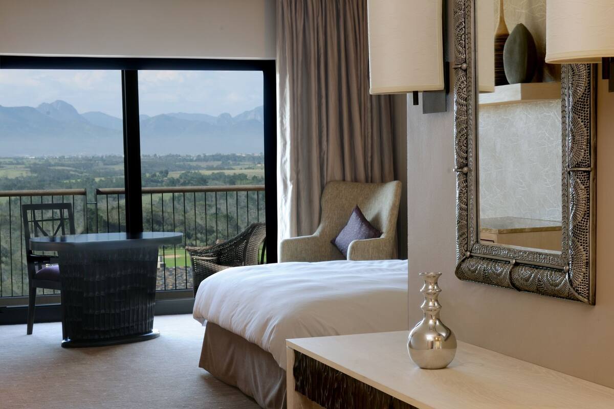 Une chambre d’hôtel comprenant un lit, un bureau, une chaise, une petite table, un vase et une vue sur l’extérieur.