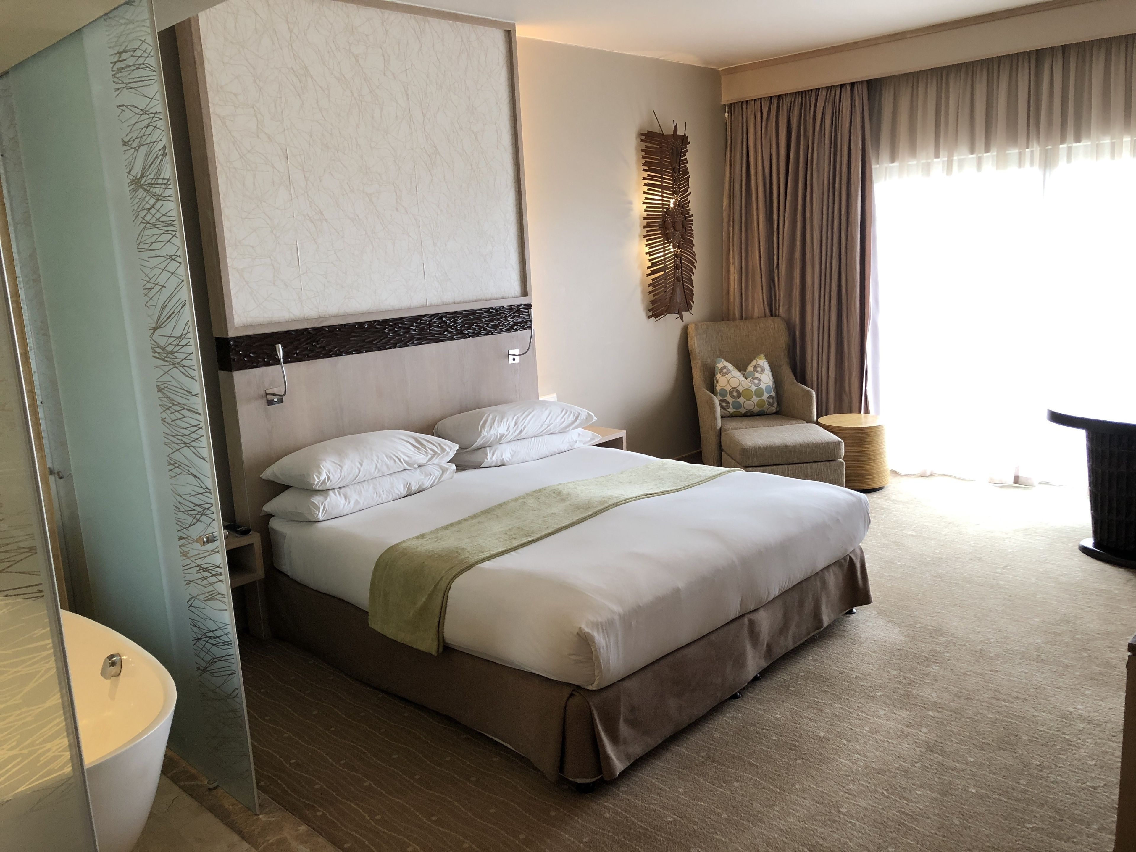 A hotel room with a large bed, a chair, a curtain, and a wall-mounted artwork.