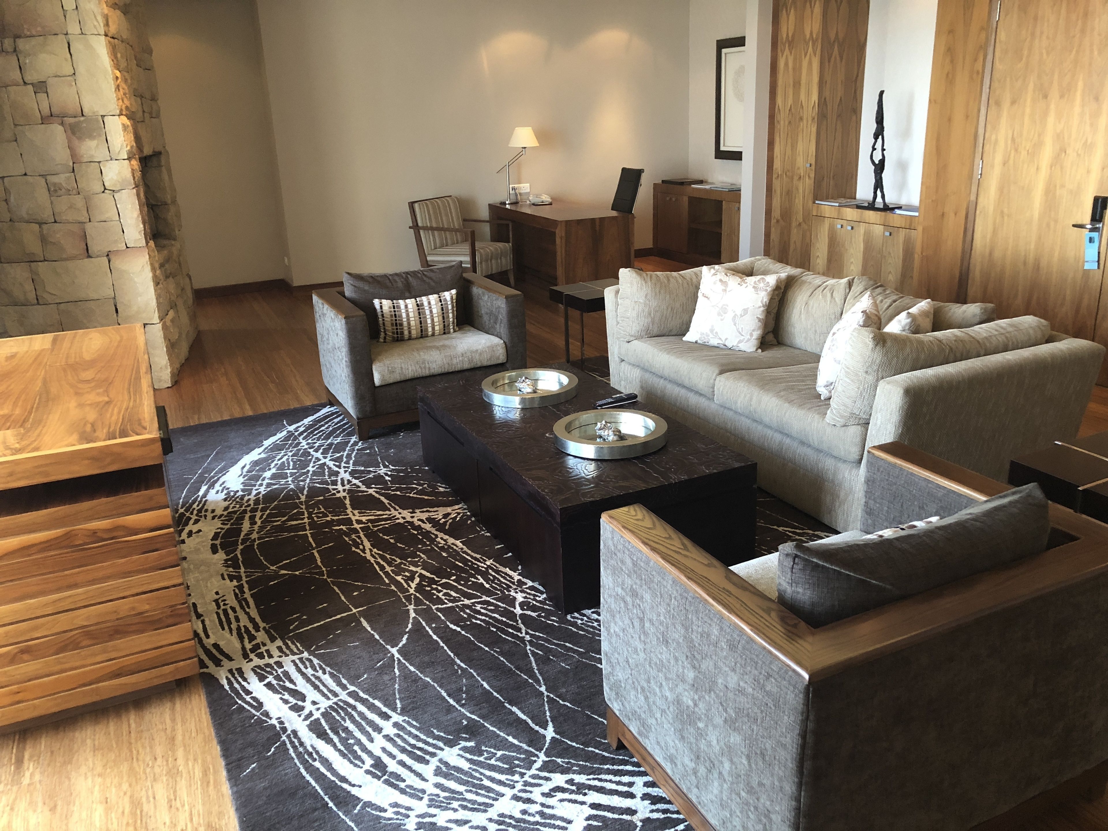 Un salon moderne avec un mur en pierre, un canapé gris, une table basse en bois et un tapis à motifs.