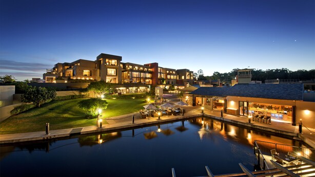 A modern hotel with a pool, outdoor seating, and a well-lit facade. - Oubaai Hotel Golf & Spa (Herolds Bay)