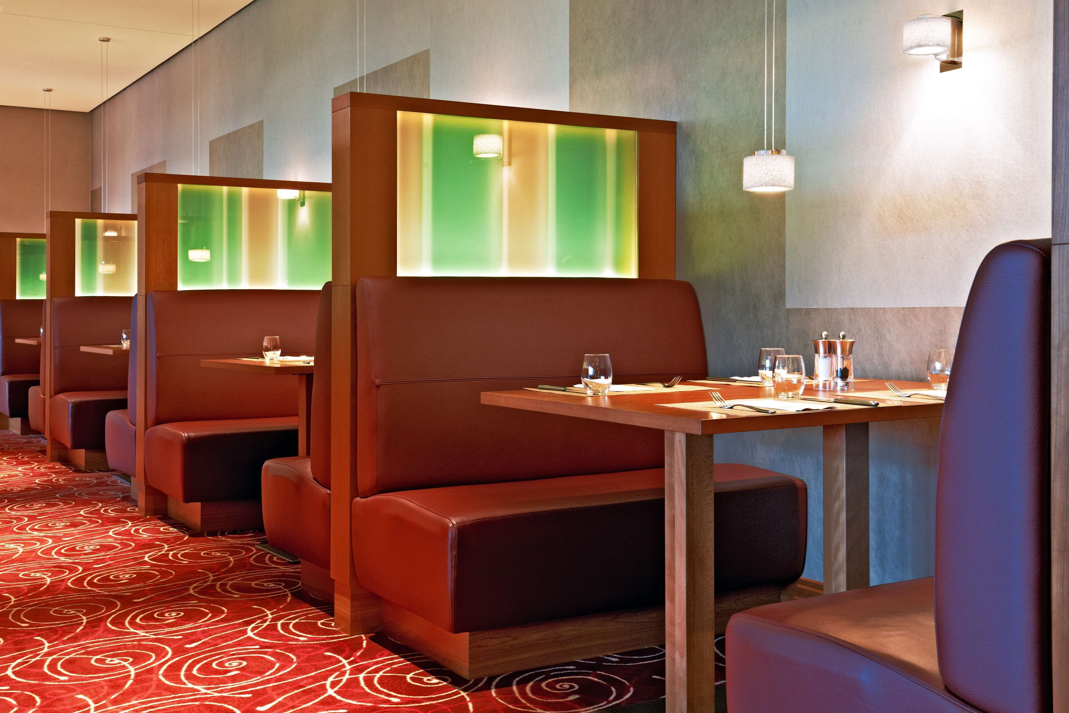 A row of booth-style seating with tables, each booth has a green-lit partition, and the floor has a red carpet with a spiral pattern.
