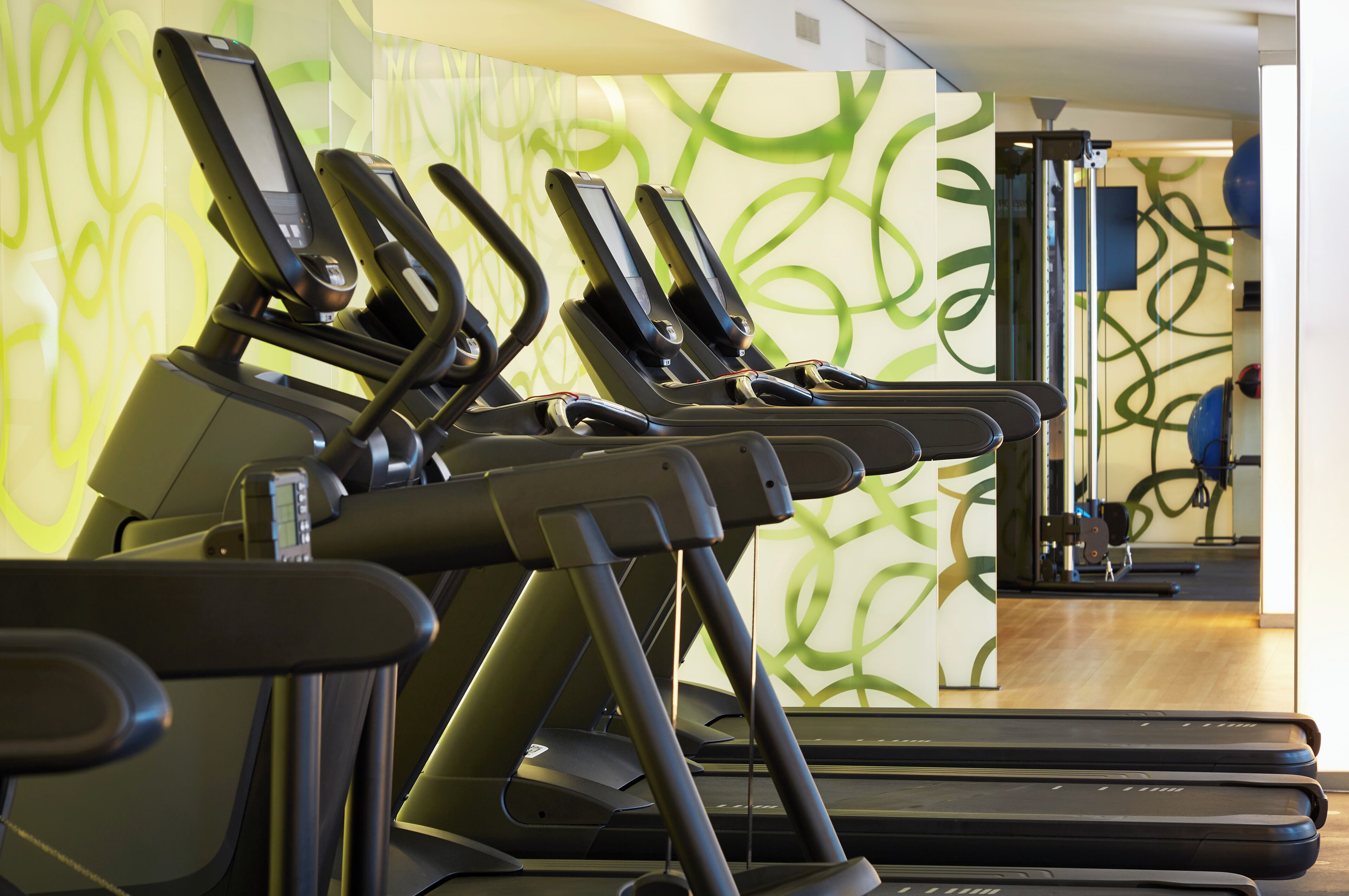 A row of stationary exercise bikes in a gym with a green abstract wall design.