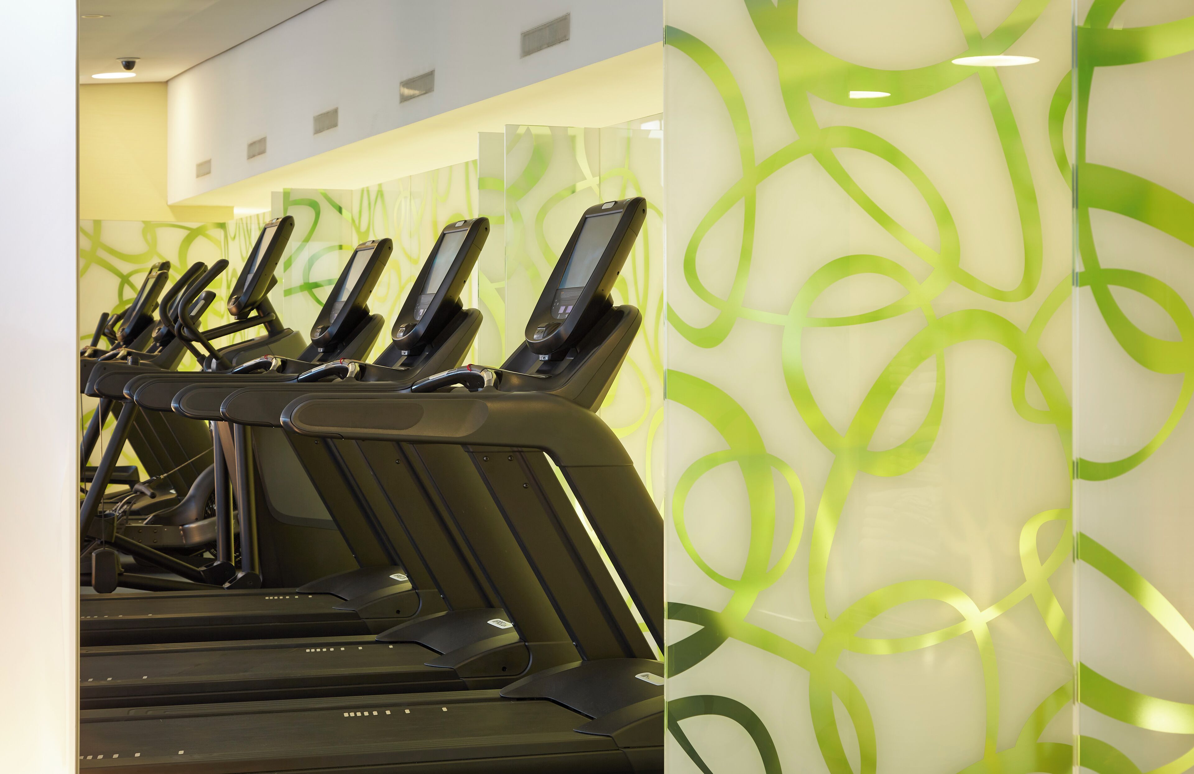 A row of treadmills in a fitness area with a modern, abstract green wall design.