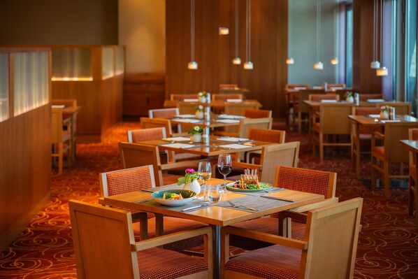 A restaurant with wooden tables and chairs, arranged in a spacious layout. - Hilton Garden Inn Frankfurt Airport (Frankfurt)