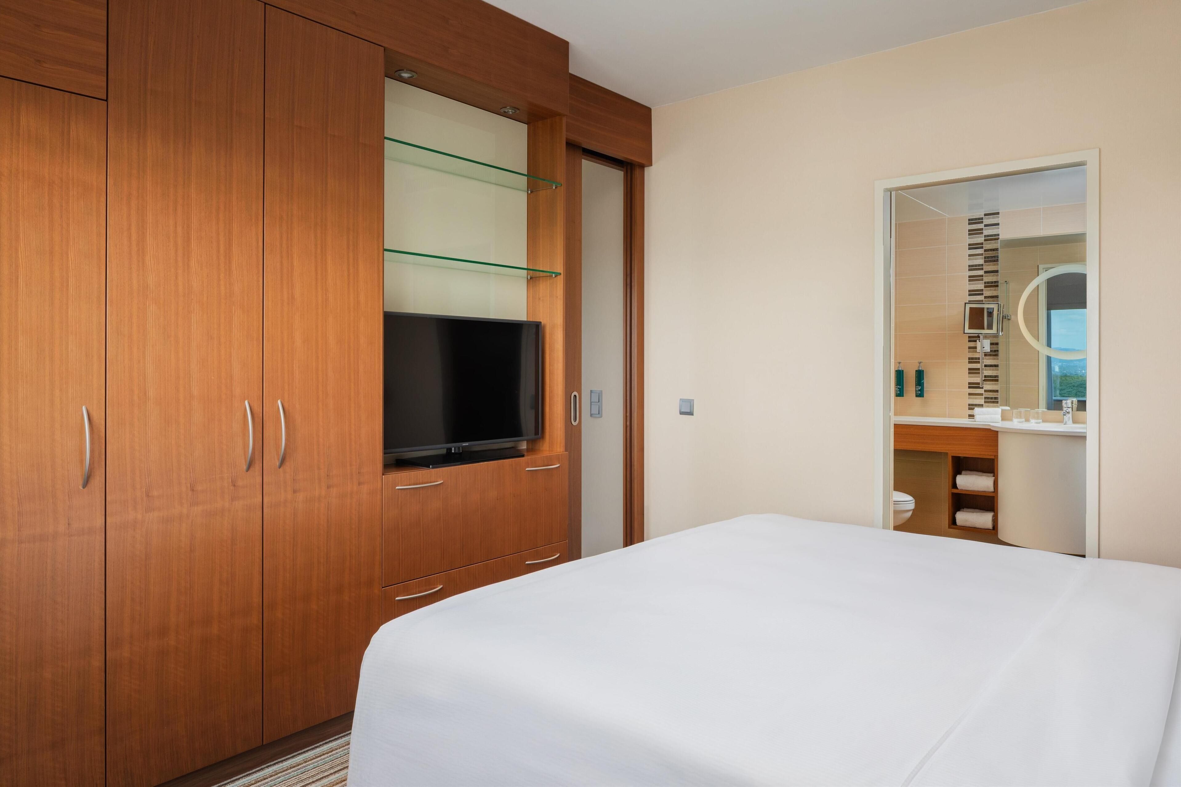 Ein Hotelzimmer mit einem großen Bett, einem Holzschrank, einem Fernseher und einem durch eine offene Tür einsehbaren Badezimmer.