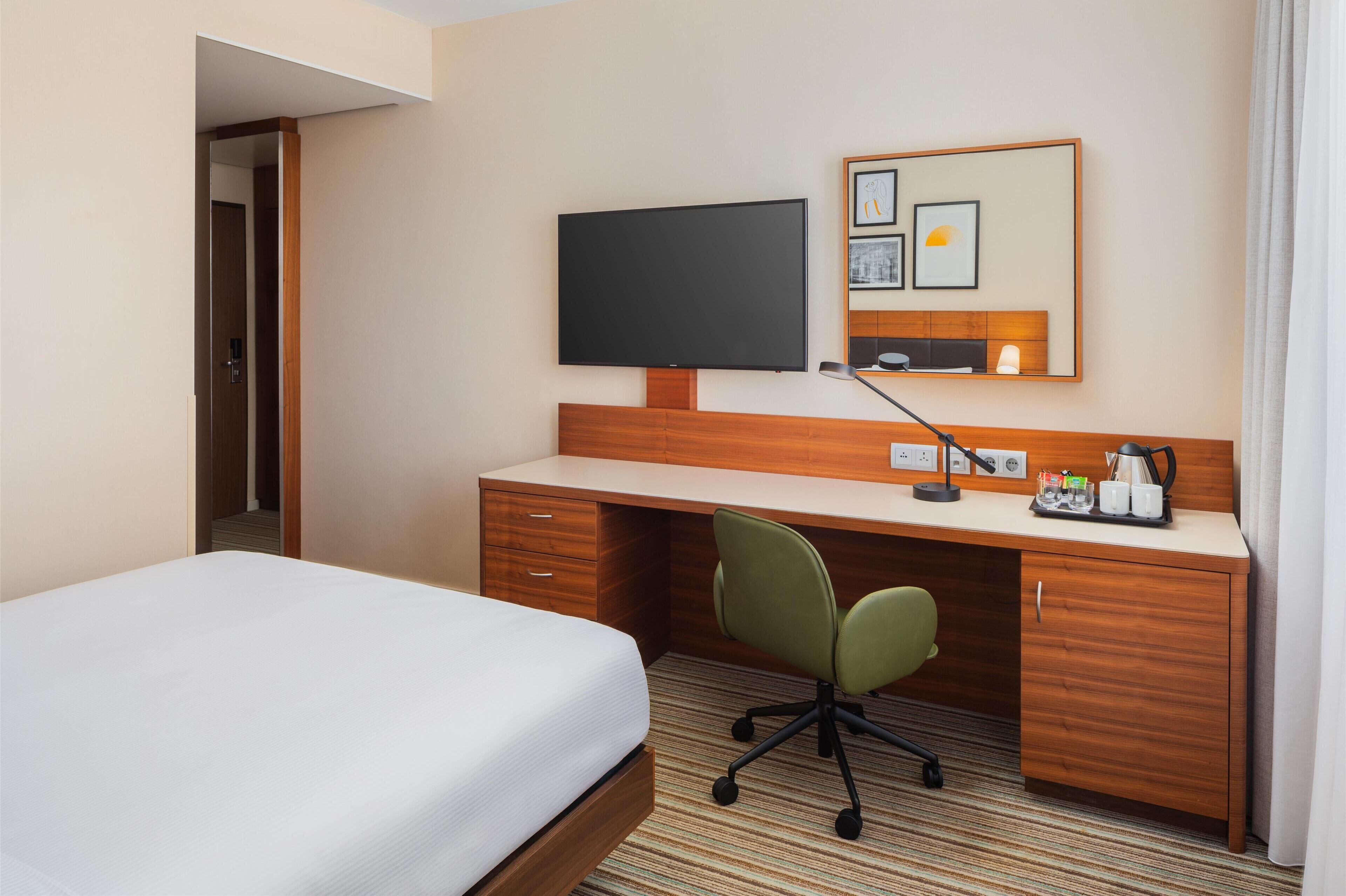 Habitación de hotel con cama, escritorio, silla, televisor y una pequeña zona para café.