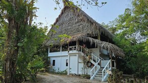 Un edificio de dos pisos con techo de paja, rodeado de follaje tropical.