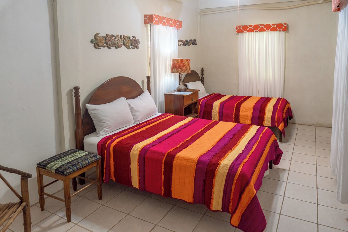 Un dormitorio con dos camas, una mesita de noche, una silla y decoración mural.