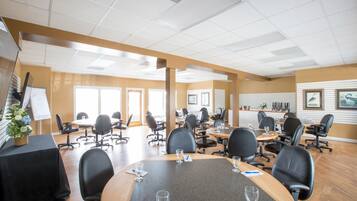 A conference room with multiple tables and chairs, a whiteboard, and a plant on a table.