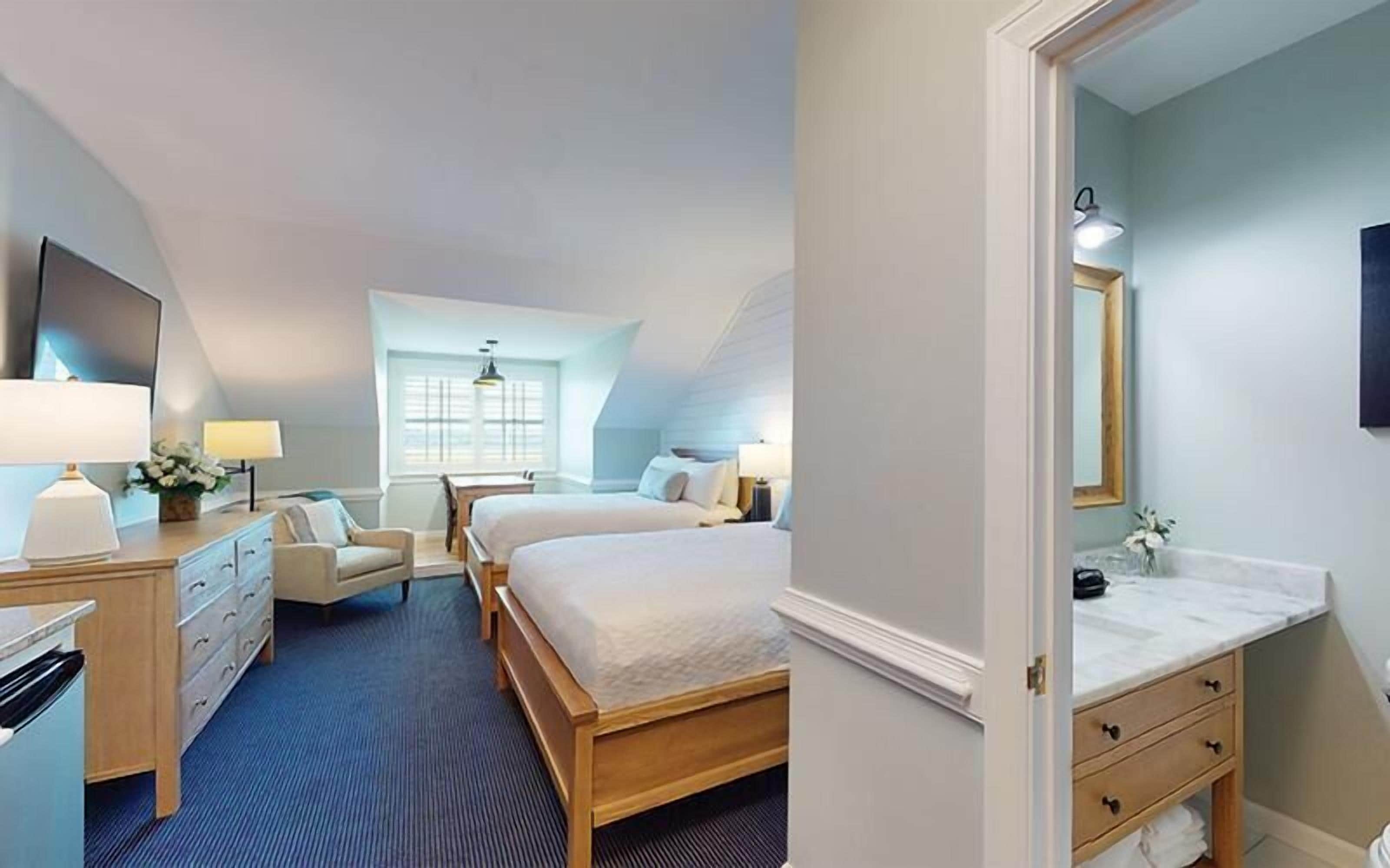 Una habitación de hotel con cama, escritorio, silla, cómoda, espejo y ventana.