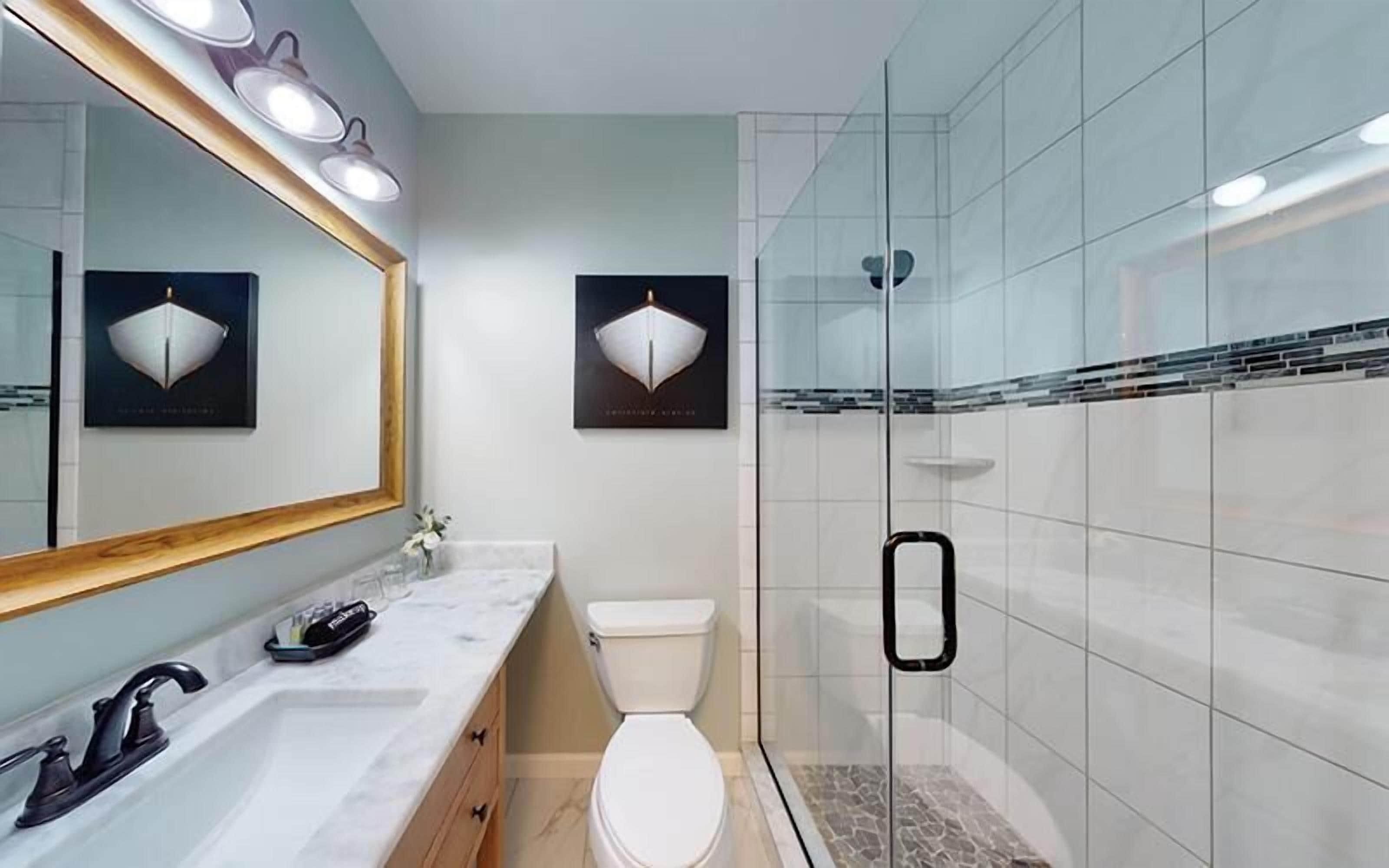 A bathroom with a marble vanity, a toilet, a glass shower enclosure, and two wall-mounted lights.